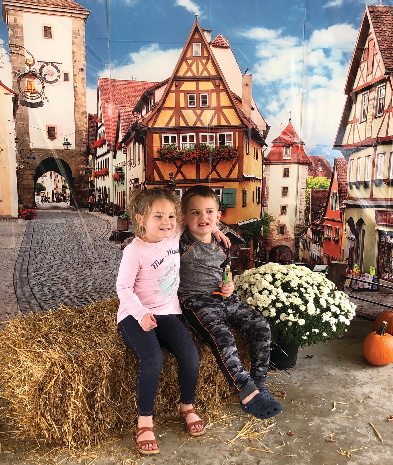 Two children pose for a picture in front of a German village backdrop.